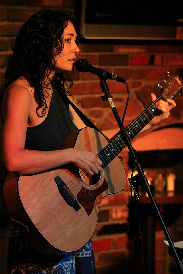 Miki Huber singing with an acoustic guitar under warm stage light